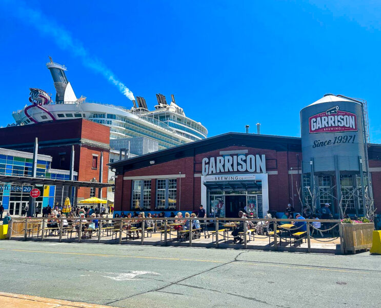 A photo of the exterior of Garrison Brewing's Seaport location. It's a sunny day with clear blue skies and the top of a cruiseshop visible behind the building.