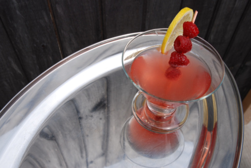 A cocktail with raspberries and lemon sitting on a tray.