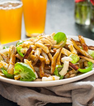 A plate of poutine garnished with brussels sprout leaves.