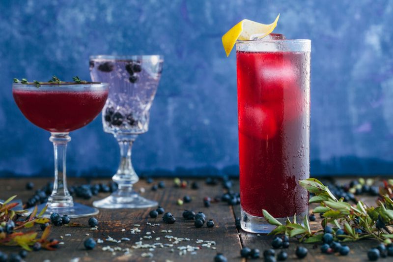 A blueberry cocktail sitting on a table surrounded by blueberries.