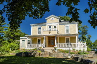 A photo of the outside of Tattingstone Inn. The inn is a pale yellow Italianate-style home, with a white porch and wooden front doors.