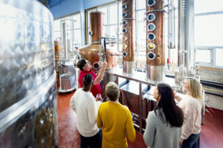 A photo of a group of four people at Steinhart Distillery looking at owner/distiller Thomas Steinhart as he shows off one of their stills.