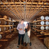 Male and female holding whiskey glasses in a barrel cellar