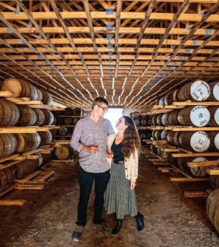 Male and female holding whiskey glasses in a barrel cellar