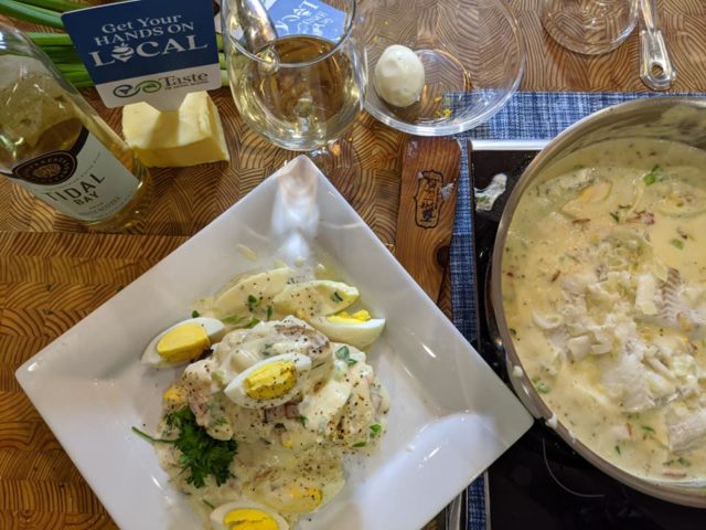 Finnan caddie sits atop a white square dish. A glass of tidal bay and a pot of finnan caddie are also seen in the shot.