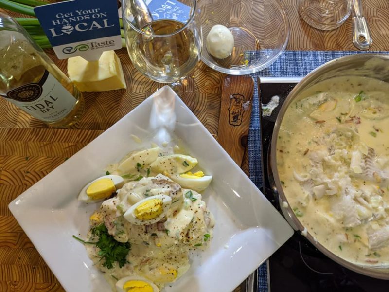 Finnan caddie sits atop a white square dish. A glass of tidal bay and a pot of finnan caddie are also seen in the shot.
