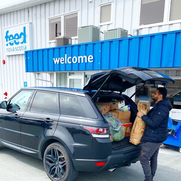 Man holds bag of potatoes with trunk of car open and filled with food as he donates to Feed Nova Scotia
