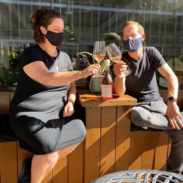 Woman and man give a wine toast while wearing masks on a patio