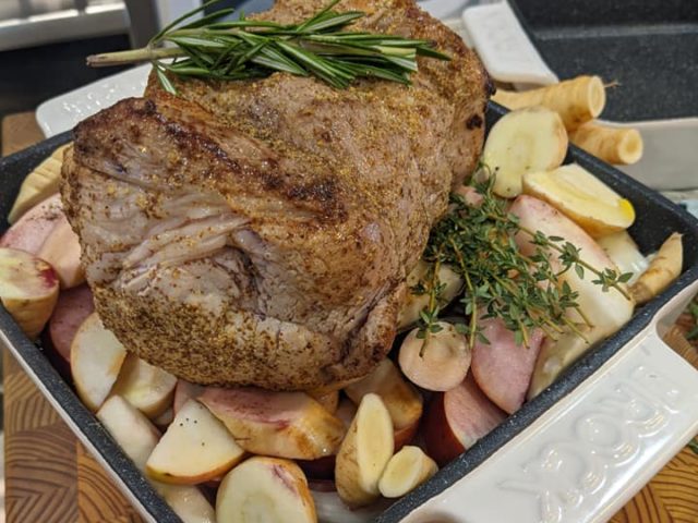 a pork roast sits atop a bed of apples, onions and parsnips in a white dish.