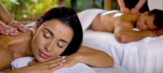 A photo of two people, one man and one woman, lying on separate massage beds. They are both having their backs massaged and look very comfortable. This photo is for Old Orchard Inn & Spa's staycation package called Couples Spa Retreat.