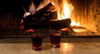 A photo of two glasses of liquor in front of a lit fireplace. This photo represents the Hot Winter Spa Night Getaway at Old Orchard Inn.