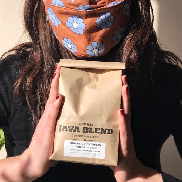 person wearing a colourful mask holds a bag of java blend coffee in their hands