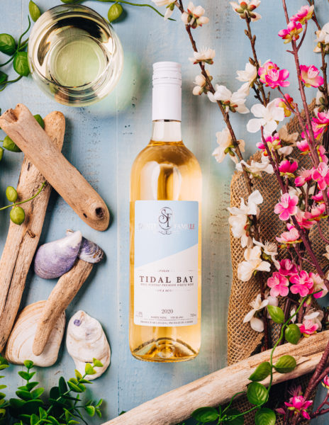 Sainte Famille Tidal Bay is laid on a table with a floral and beach themed background 
