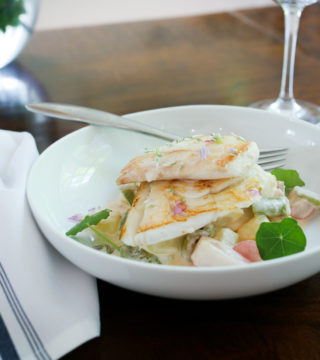 two pieces of haddock are placed in a white dish with a napkin to the left.