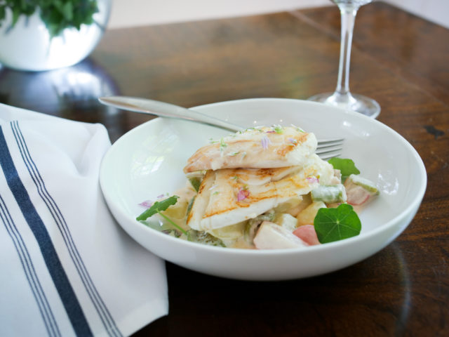 two pieces of haddock are placed in a white dish with a napkin to the left.