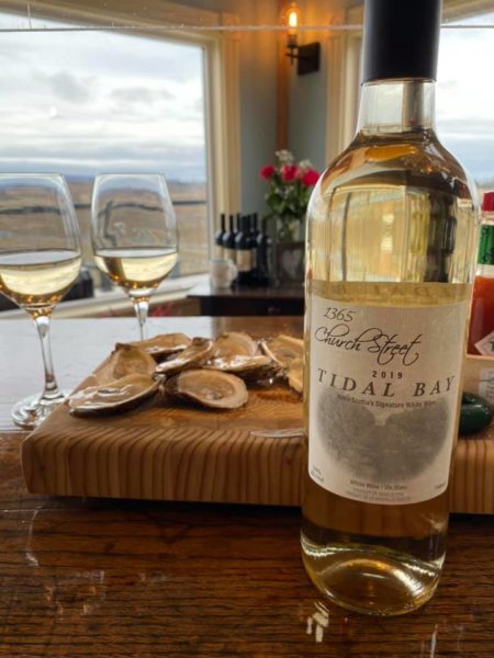1365 church street tidal bay bottle with a backdrop of two glasses of wine and a grazing board with oysters on the half shell. 