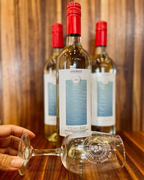 three bottles of the 2020 luckett tidal bay are set against a wooden background. There is a wine glass in front laying down. 