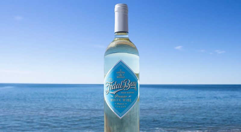a bottle of lightfoot and wolfville tidal bay sits against a backdrop of the ocean