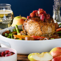 Pork roast with cider chutney on top. Sitting in white platter with a glass of Bulwark cider in background.