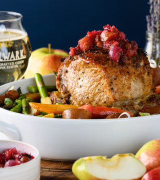 Pork roast with cider chutney on top. Sitting in white platter with a glass of Bulwark cider in background.