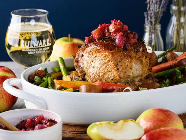 Pork roast with cider chutney on top. Sitting in white platter with a glass of Bulwark cider in background.