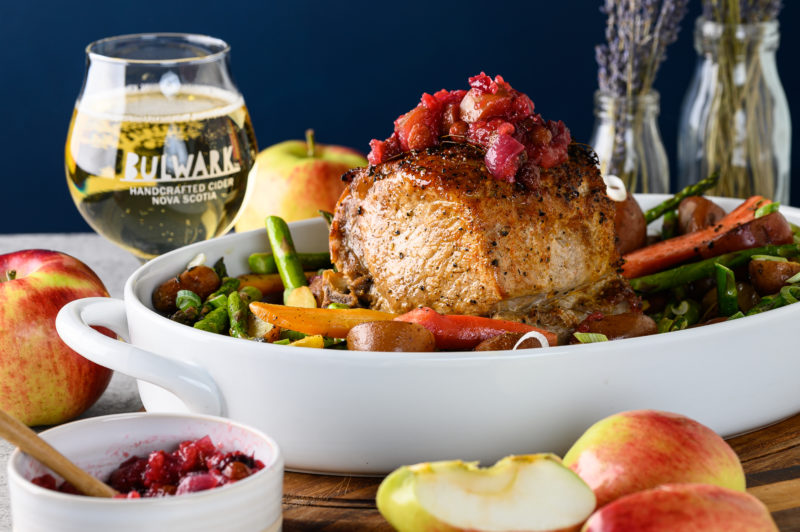 Pork roast with cider chutney on top. Sitting in white platter with a glass of Bulwark cider in background.