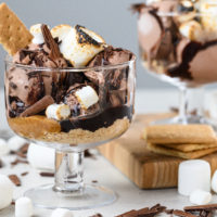 Two sundaes sit in clear bowls. Marshmallows and chocolate are scattered throughout the image.