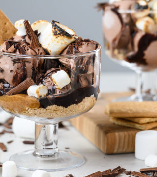 Two sundaes sit in clear bowls. Marshmallows and chocolate are scattered throughout the image.