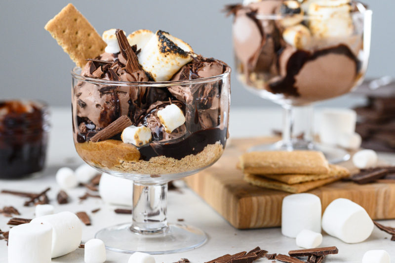 Two sundaes sit in clear bowls. Marshmallows and chocolate are scattered throughout the image.
