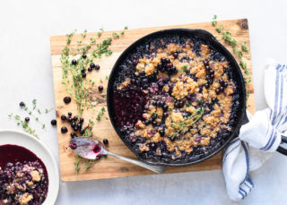 Blueberry crisp in cast iron pan on top of wooden cutting board