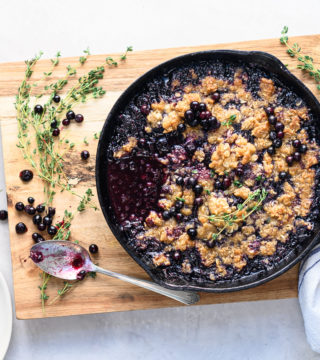 Blueberry crisp in cast iron pan on top of wooden cutting board