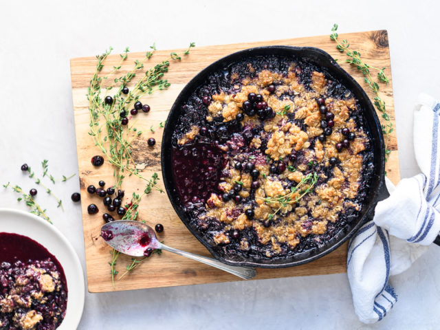 Blueberry crisp in cast iron pan on top of wooden cutting board