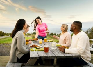 Four people sit at a picnic table while they're served by someone in a pink shirt