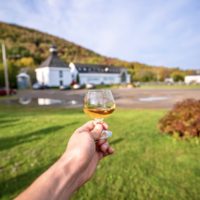hand holds a dram of whiskey in front of glenora