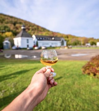 hand holds a dram of whiskey in front of glenora