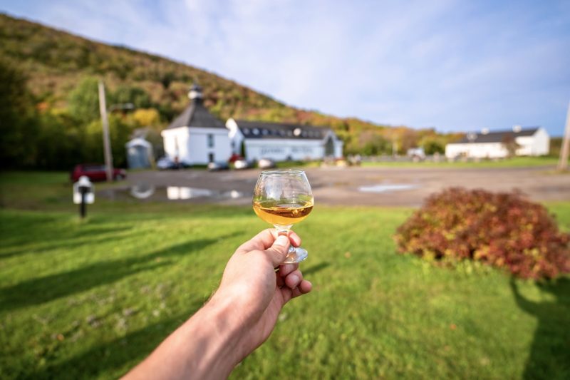 hand holds a dram of whiskey in front of glenora