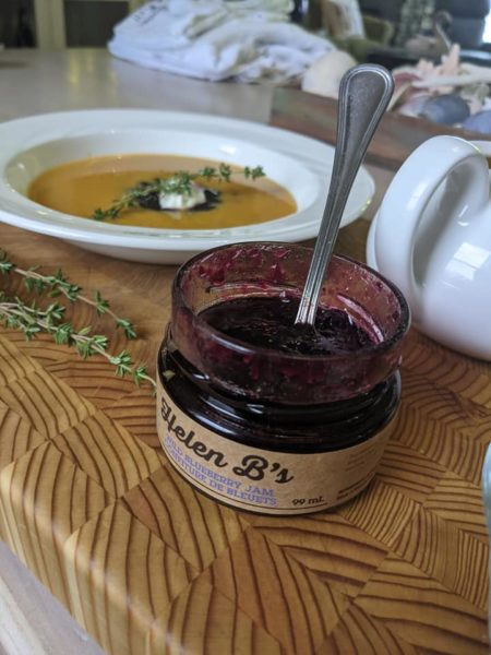 jar of helen b's blueberry jam sits on wooden cuting board with bowl of soup in background