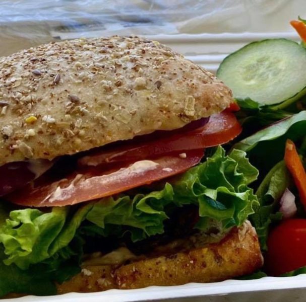 a sandwich with tomato and lettuce sits next to a salad with cucumber