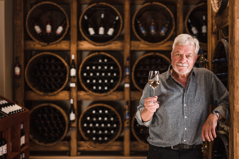 A man holds a glass of white wine in a wine cellar
