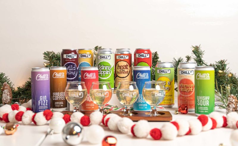 Several cans of cider are lined against a wall. There are tasting glasses in front. 