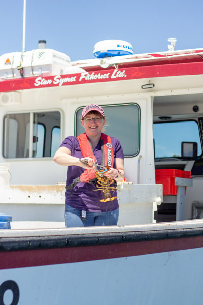 Woman holds lobster on site of fishing boat