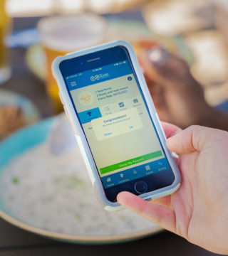 A hand holds a phone with the Taste of Nova Scotia app open over a bowl of chowder