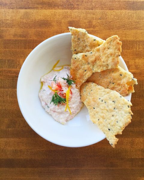 A white bowl holds snow crab dip and crisps on a wooden counter