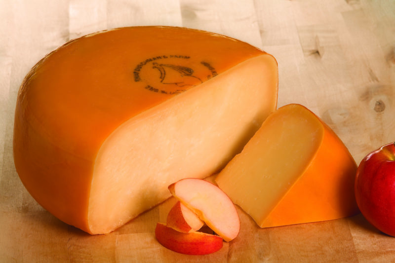 A photo of Old Grower Gouda cheese produced by That Dutchman's Cheese Farm. There is half a wheel of cheese in the photo.