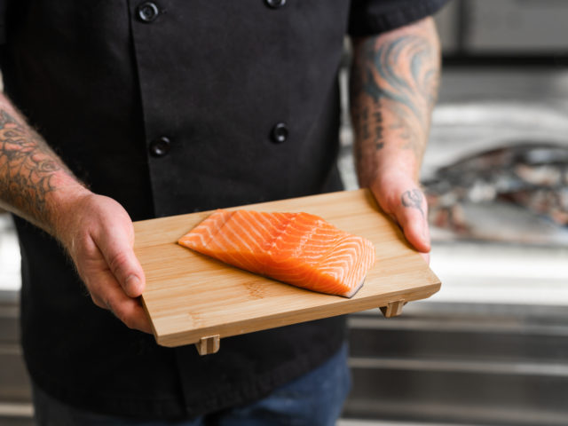 hands hold salmon on a board