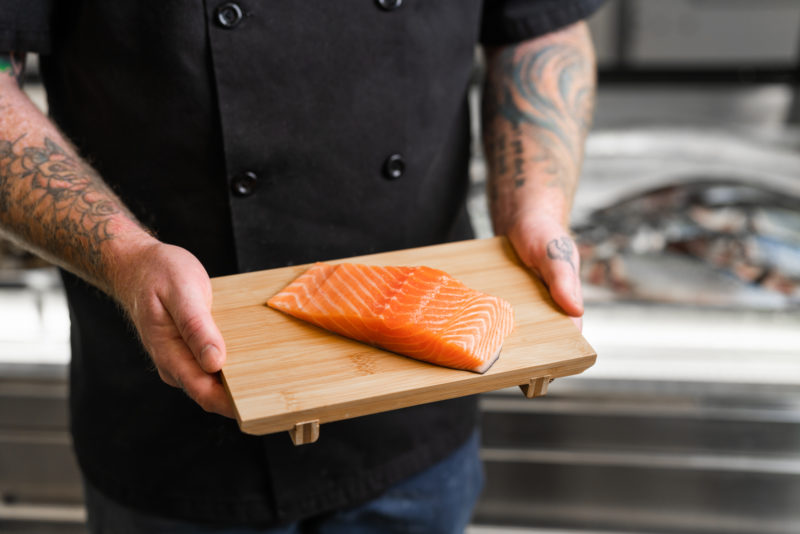 hands hold salmon on a board