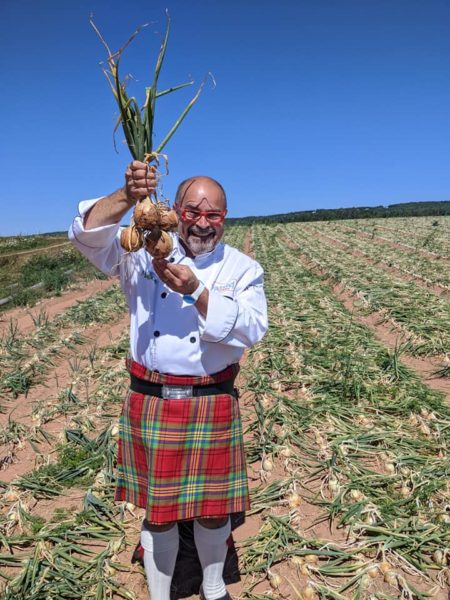 the kilted chef in a kilt stands in a field of onions, holding onions