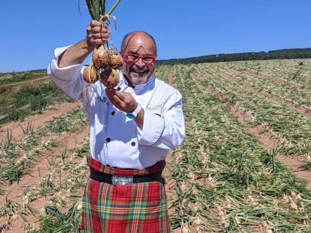 the kilted chef in a kilt stands in a field of onions, holding onions