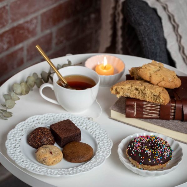 several treats sit in plates on a table including cookies and brownies. There is also a white mug of tea. 