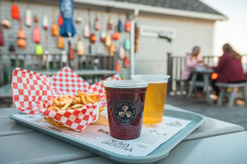 Two beers and fries sit on a tray on a picnic table. There are buoys on a wall in the background